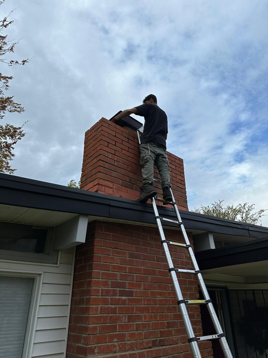 Technician on a ladder inspecting a brick chimney at the roofline