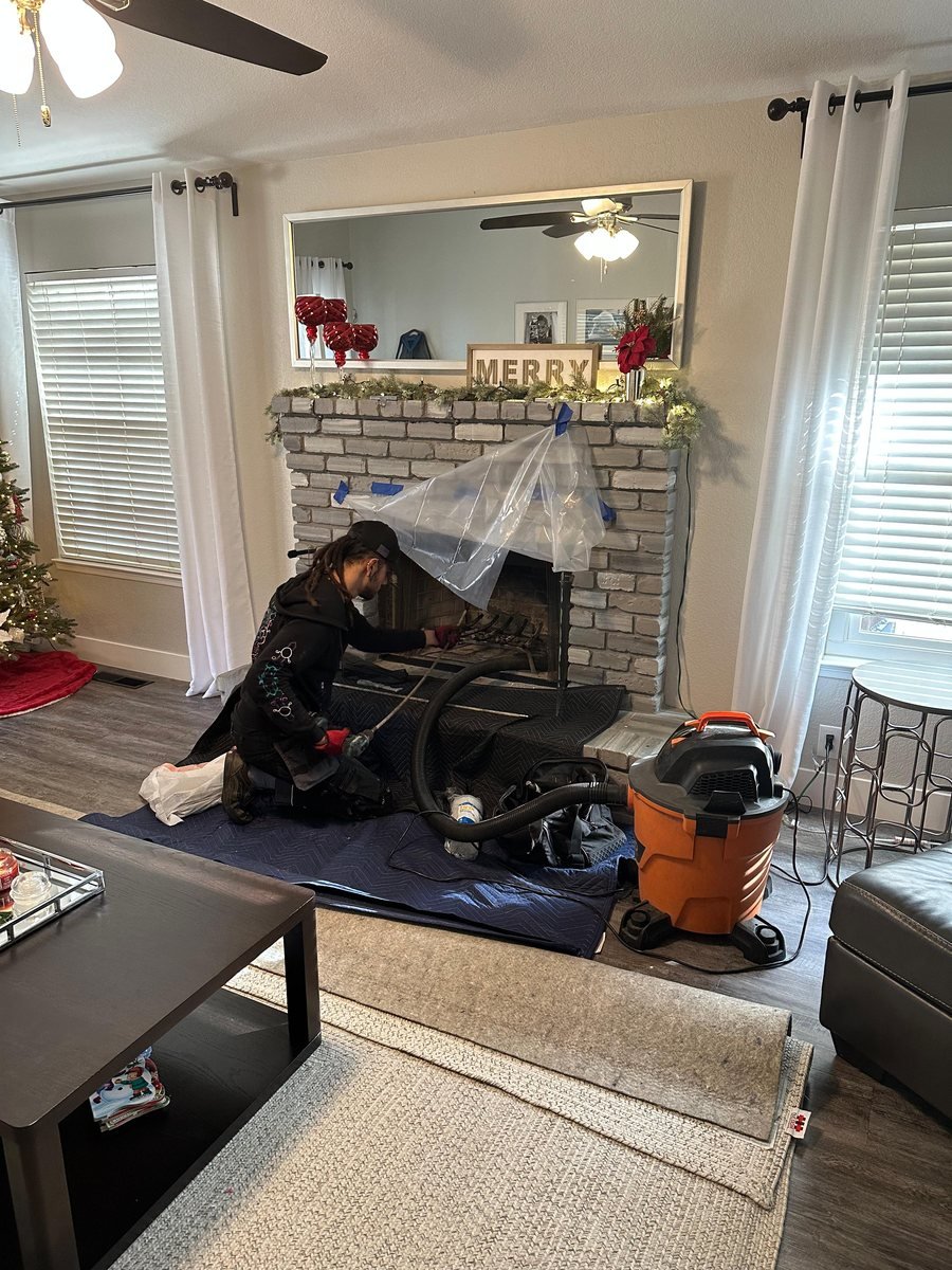 Baker Chimneys technician sweeping a living room fireplace with the hearth and floor sheeted off