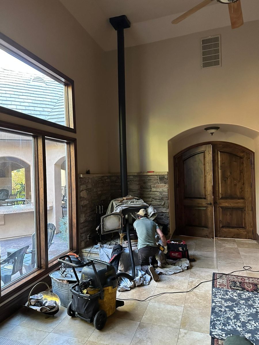 Technician servicing a freestanding wood stove with drop cloths and a vacuum