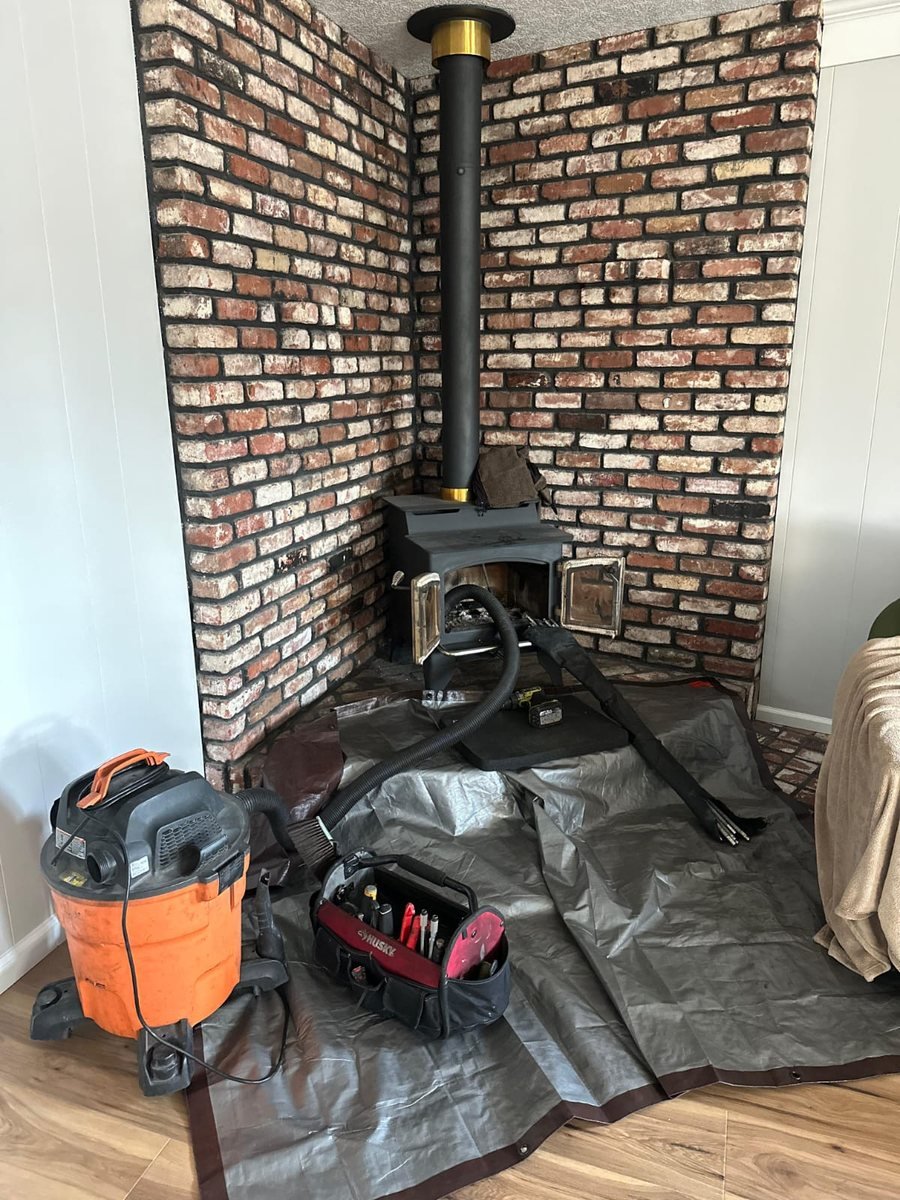 Wood stove in a brick alcove pulled forward for a flue sweep